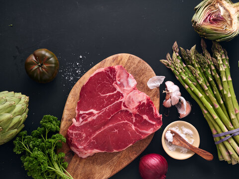 Raw t-bone steak on wooden board with fresh vegetables