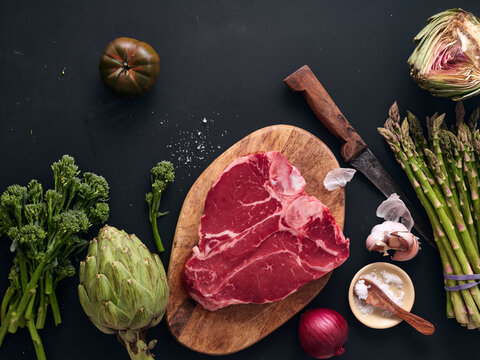 Raw t-bone steak on wooden board with vegetables and knife