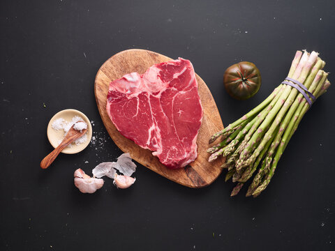 Raw t-bone steak with fresh vegetables on wooden board