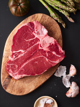 Raw t-bone steak on wooden board with garlic, vegetables