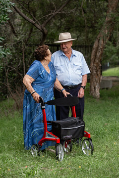 Elderly woman using a walker talking to an elderly man outdoors among the trees