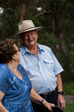 Caucasian elderly woman standing close with an elderly man, conversing outdoors among green trees