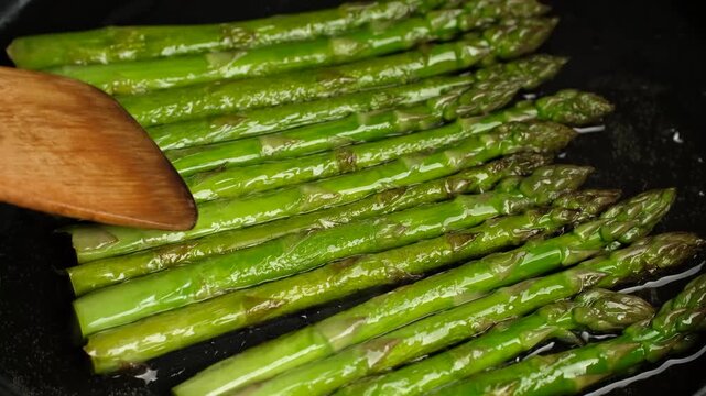 Process frying green asparagus in pan. Healthy vegan food concept