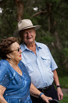 Elderly woman in patterned blue dress with sunglasses talking to elderly man