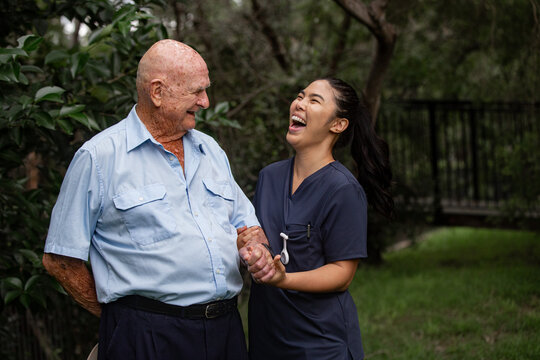 Australian elderly man holding hands with Filipina caregiver in navy scrubs