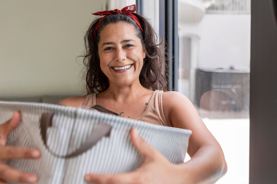 Smiling woman holding laundry basket at home in daylight