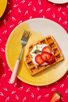 Waffle topped with strawberries and cream on a plate