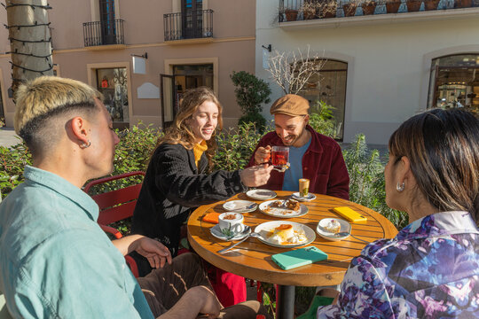 Friends sharing dessert and tea on a sunny terrace cafe