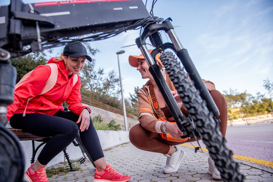 Two women friends check electric bicycle before urban ride