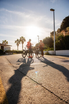 Two friends pause with electric bicycles on a sunny coastal street