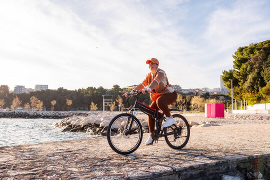 Woman riding electric bicycle on seaside promenade at sunset