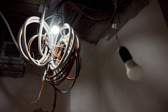 Damaged electrical cables hanging from concrete ceiling in building. Building renovation area featuring unsafe wiring and inadequate safety measures during construction