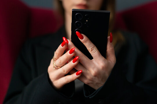 Woman using smartphone at work with red manicure closeup