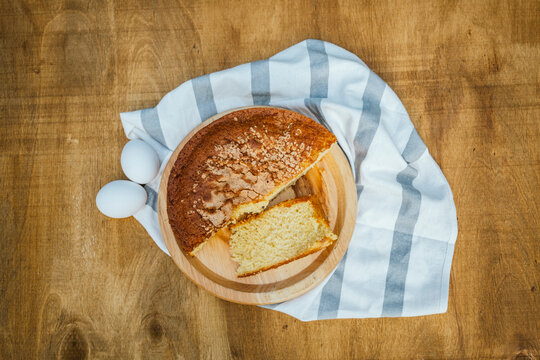 Overhead view of homemade sponge cake slice on wooden board with eggs