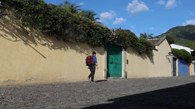 backpacker walking down scenic colonial street in antigua guatemala (backpacking latin america with large backpack) book bag back pack spanich architecture scenic tropical city