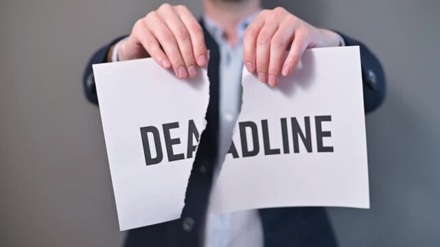 An adult male in a suit tears a paper labeled deadline in front of a plain background. This action symbolizes the relief of getting rid of pressure and stress from deadlines