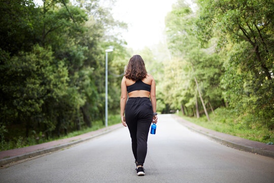 Back view of woman walking on a forest road with water