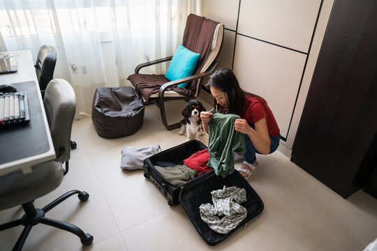 Asian woman packing suitcase at home with pet dog nearby