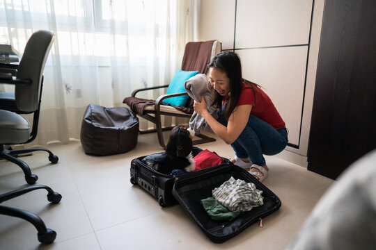 Asian woman packing suitcase and bonding with pet dog