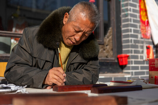 Elderly Chinese man practicing traditional calligraphy outdoors