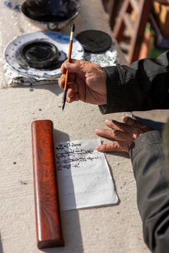 Elderly hands practicing Chinese calligraphy with brush and ink