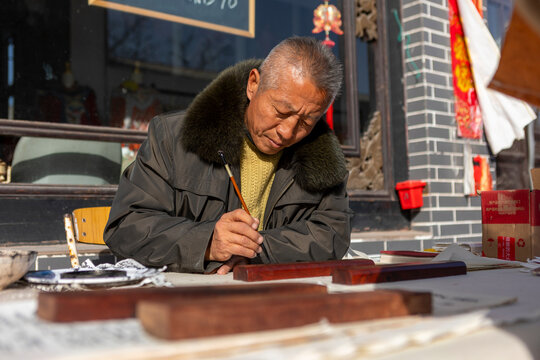 Elderly man practicing Chinese calligraphy at outdoor table