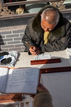 Elderly man practicing Chinese calligraphy with brush outdoors