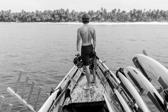 Surf photographer on wooden boat facing tropical shore