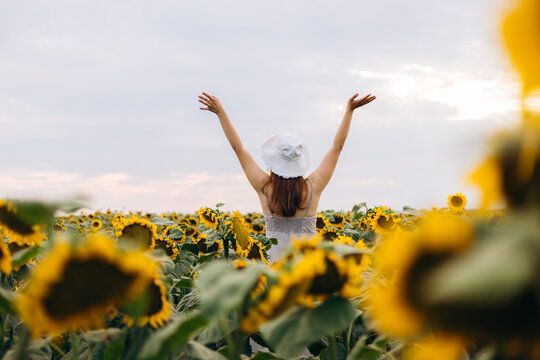 Woman with raised arms in sunflower field under cloudy sky