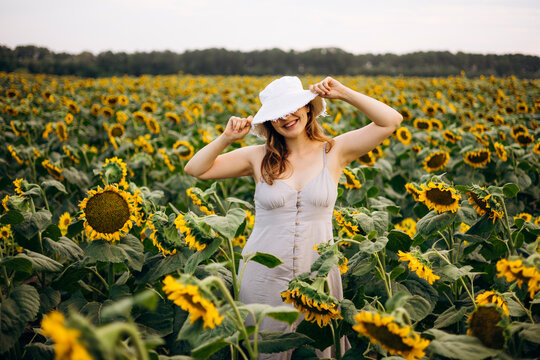 Woman in white hat smiling in blooming sunflower field