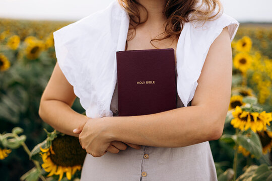 Woman holding Holy Bible in sunflower field, faith concept