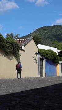backpacker walking down scenic colonial street in antigua guatemala (backpacking latin america with large backpack) book bag back pack spanich architecture scenic tropical city