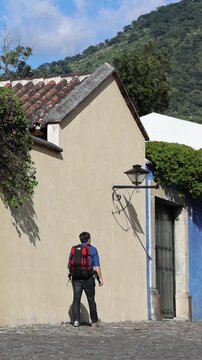 backpacker walking down scenic colonial street in antigua guatemala (backpacking latin america with large backpack) book bag back pack spanich architecture scenic tropical city