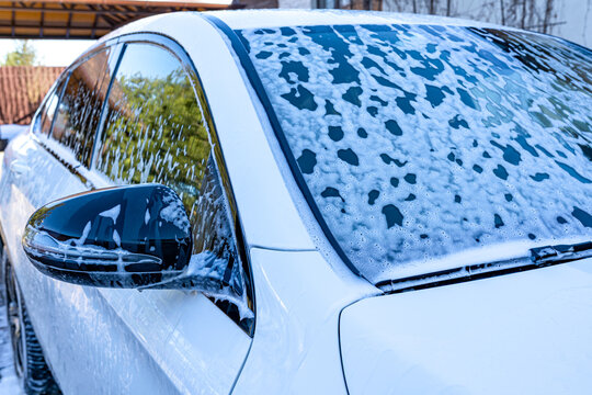 Close-up of white car covered in soap foam during wash