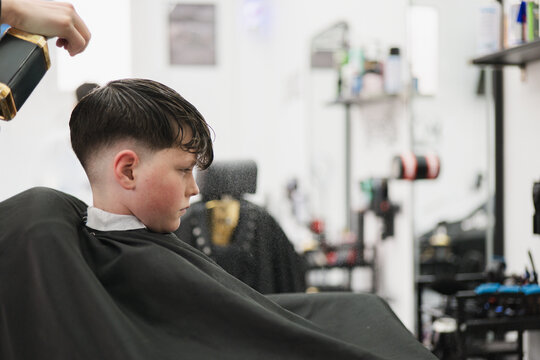 Boy getting haircut with spray in modern barbershop