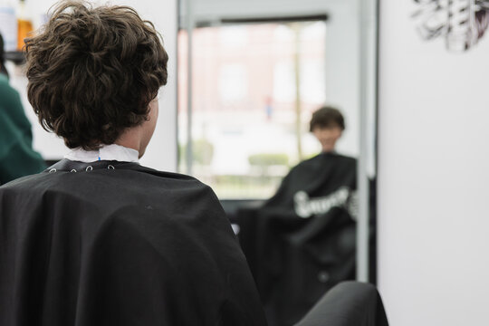 Boy getting haircut in barbershop, looking in mirror