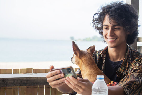 Young man taking a selfie with his phone with his adorable dog on his lap on an outdoor bar terrace