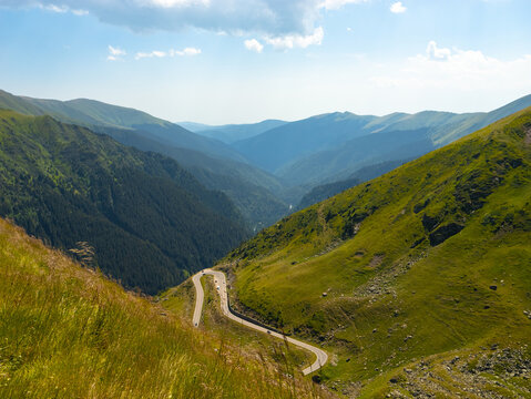 Winding through the Carpathian Mountains, the Transfagarasan route showcases breathtaking green hills and deep valleys under a clear blue sky.