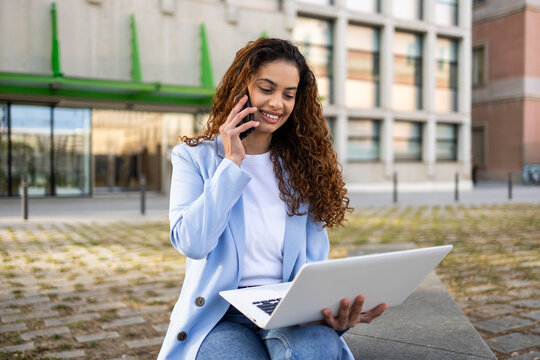 Businesswoman using laptop and phone call outside office