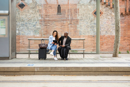 Business couple using tablet at transit stop with luggage