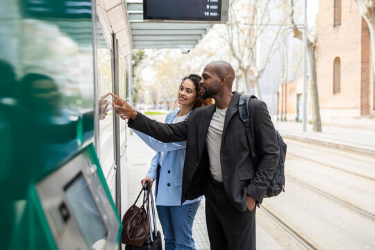 Business couple checking schedule at tram stop on trip