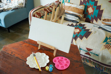 Fototapeta premium Blank Canvas on Easel with Paint Supplies in Living Room