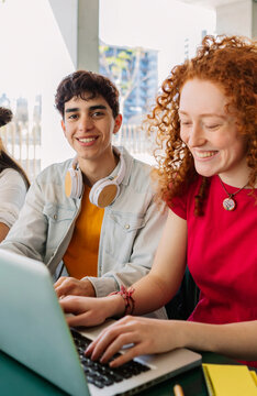 Vertical shot of young male student smiling at camera while studying in group at high school. Education concept