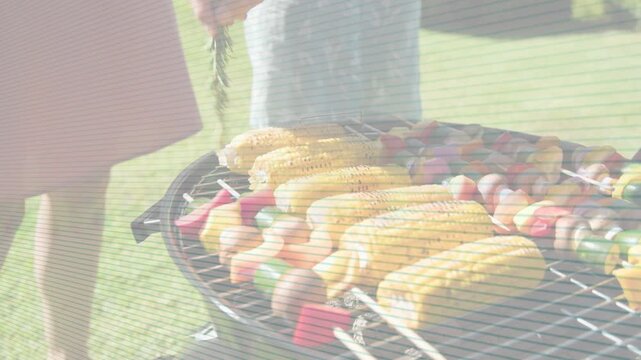 Man at grill dipping into bowl basting corn and turning ears lining skewers for even cooking