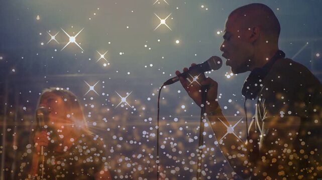 Lead singer on music cue leaning mic singing reaching up band singing under sparkles engaging fans