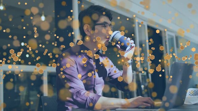 Man lifting coffee cup, sipping while typing on laptop for focus in business, golden bokeh drifting