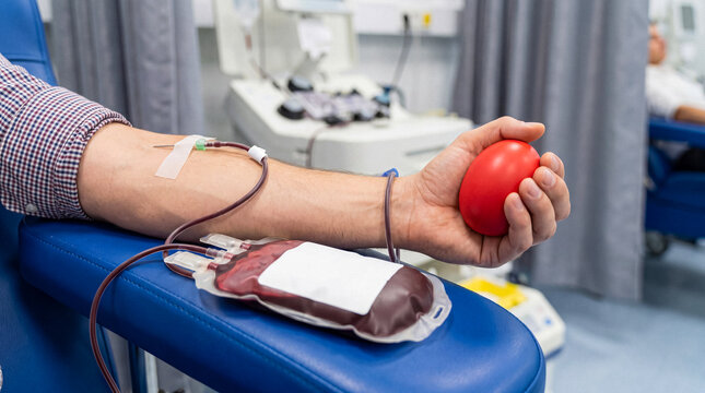 Close-up of a male donor's arm as he donates blood in a hospital, holding a red stress ball during the process.
