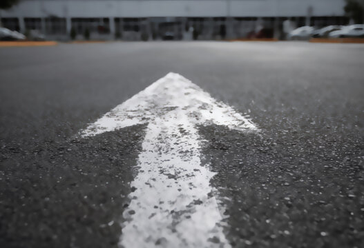 White directional arrow painted on asphalt, pointing forward into a blurred background