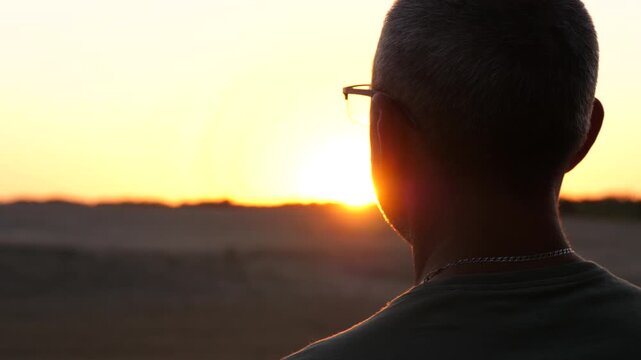 Man watching sunset in serene landscape, enjoying quiet moment of solitude and reflection. Golden hour light highlights mindfulness, mental reset and peaceful connection with nature.