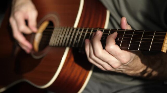 Acoustic guitar playing at home. Musician strums chords with passion. Natural light creates warm atmosphere. Intimate setting inspires creativity and relaxation.